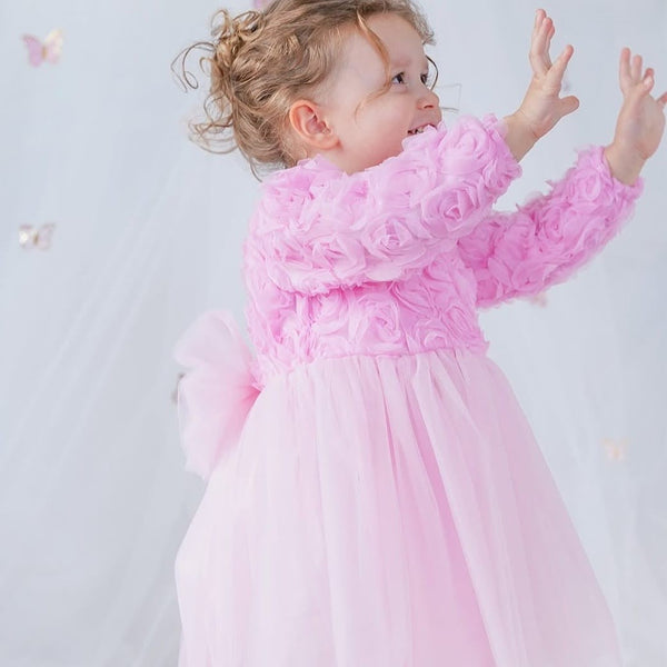 Child wearing a pink dress with floral details against a light background